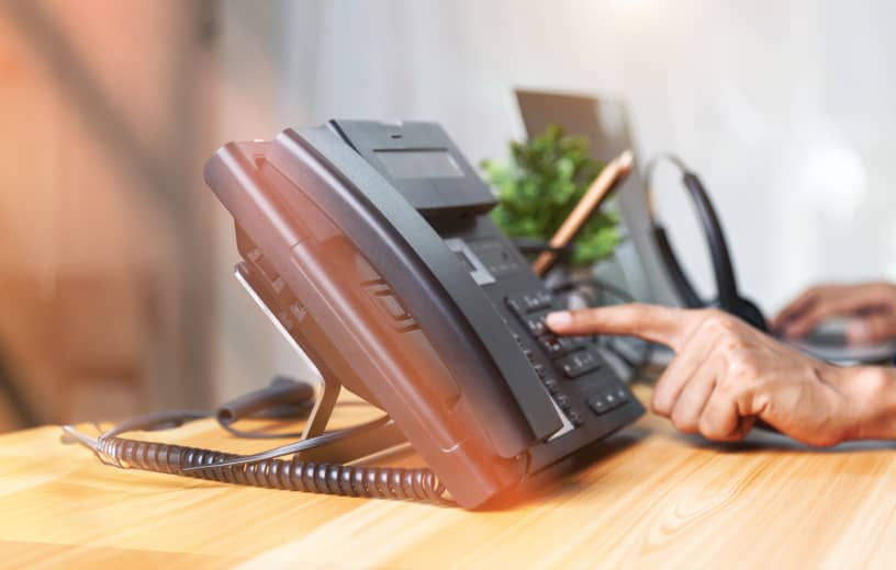 A hand pressing buttons on an IP desk phone