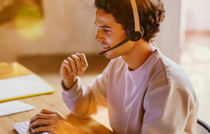 A smiling man wearing an IP headset is typing on his laptop