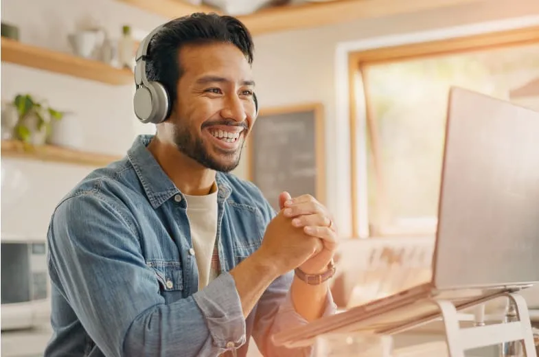 A smiling man with headphones on in fron of his laptop
