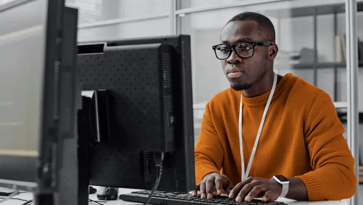 A man looking at his monitor screen while typing on a keyboard